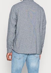 Dlouhý rukáv košile světle modré barvy s texturovaným vzorem, s límečkem a manžetami na knoflíky, v kombinaci se světle modrými džínami.