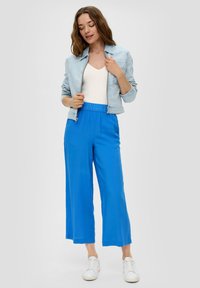 Lichtblauwe denimjack over een witte strakke top, gecombineerd met felblauwe wijde broek en witte sneakers. Soepele texturen en een relaxte pasvorm.