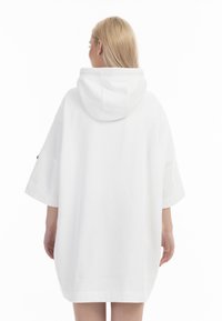 Rochie hoodie albă, supradimensionată, cu glugă, mâneci scurte și o croială lejeră, având o textură fină și un design minimal.