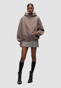 Oversized taupe hoodie with a front pocket, paired with a patterned mini skirt, black knee-high socks, and ankle boots.