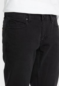 Jeans negri din denim cu un design ajustat, având buzunare frontale și închidere cu nasture. Textură netedă și detalii de cusătură subtile.