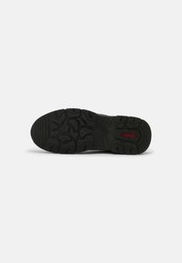 Black rubber shoe sole featuring a textured tread pattern with varying shapes for grip. Logo in red near the heel area.