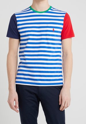 Mand iført en kortærmet T-shirt med blå og hvide vandrette striber, én marineblå og en rød ærme samt en grøn krave.
