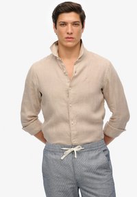 Lichtbeige linnen overhemd met een knoopsluiting bij de kraag en opgerolde mouwen, met een subtiele textuur en een klein geborduurd logo.