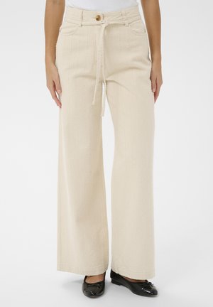 Pantalon crème à jambes larges avec rayures texturées verticales, taille à bouton et cordon, porté avec des ballerines noires vernies.