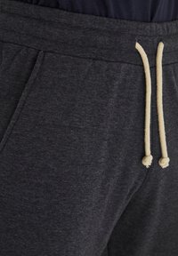 Pantalons de survêtement gris foncé en tissu doux, avec une taille à cordon de serrage et des accents beiges ainsi que des poches latérales.