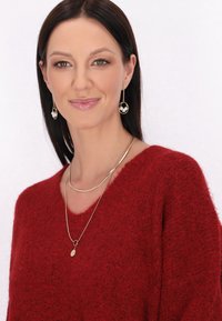 Pulover roșu pufos cu decolteu în V. Cercei de aur; unul are un pandantiv oval, plat. Cercei cerc de aur cu perle. Material moale, texturat.