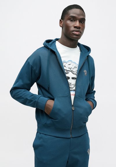 Tmavý tyrkysový mikina s kapucňou na zips, s rebrovaným lemom a manžetami, s logom uprostred na hrudníku a dvoma prednými vreckami.