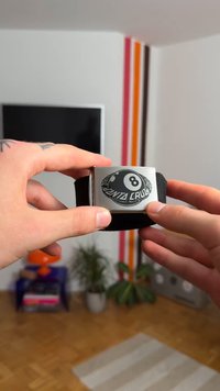 Svart stoffarmbånd med en sølv rektangulær spenne. Spenna viser et svart 8-ball grafikk med teksten "Santa Cruz".