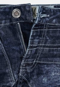 Jeans in denim blu scuro con chiusura a zip, bottone metallico e cuciture a contrasto. Presenta cinque tasche e una finitura sfumata.