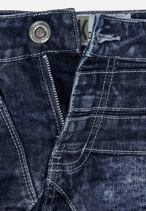 Jeans in denim blu scuro con chiusura a zip, bottone metallico e cuciture a contrasto. Presenta cinque tasche e una finitura sfumata.