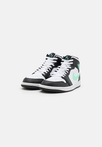 Czarno-białe sneakersy za kostkę z zielonymi akcentami, z perforowanym noskiem, białymi sznurówkami i gumowymi podeszwami o teksturowanym wzorze.
