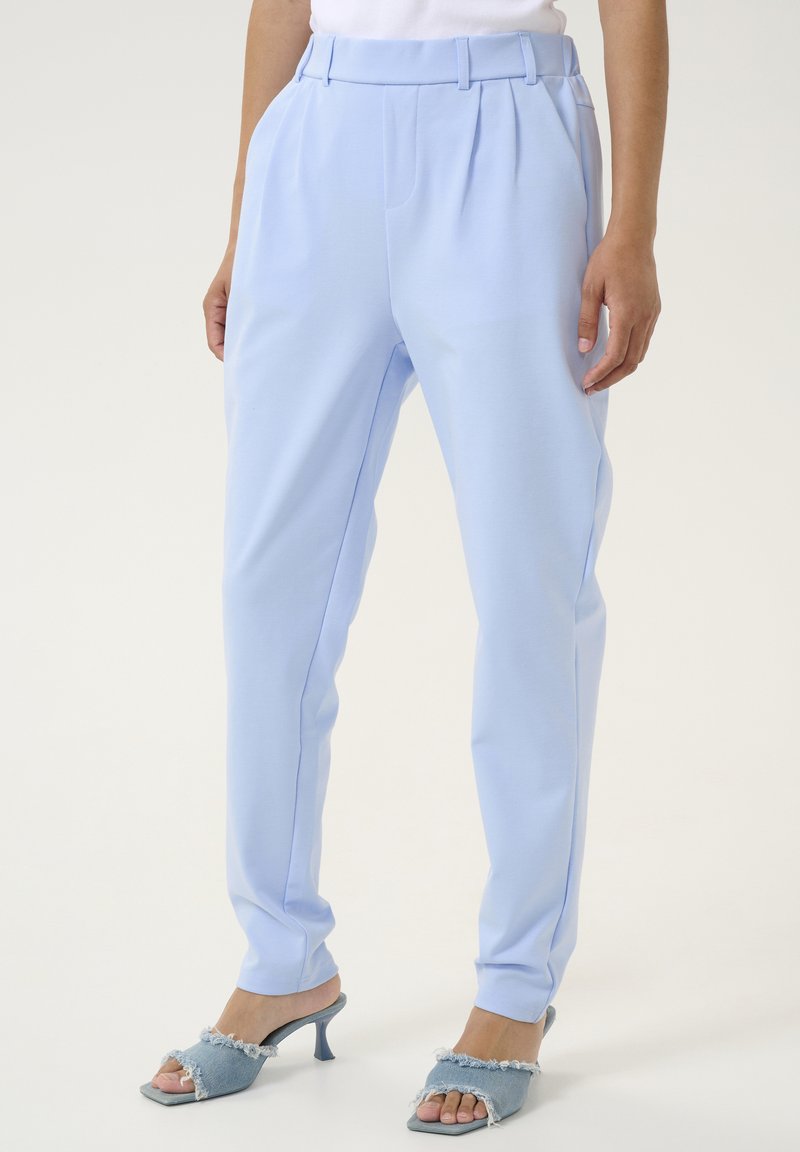Svetlo modre hlače s pregibi, krojeno prileganje in gladko teksturo. Ujemajoče svetlo modre sandale s peto z raztrganimi denim akcenti.