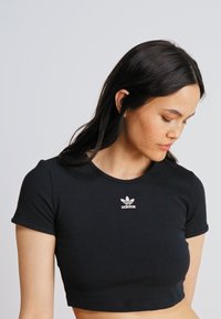Must кардаs T-särk, mis on valmistatud ribakangast, väikese valge Adidas'i logoga rinnal, ümmarguse kaelakaeluse ja lühikeste varrukatega.