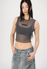 Pilkos permatomos trumpųjų palaidinių, ant kurių užrašytas žodis "Ragged" juodu šriftu, derinamos su raštuotomis džinsinėmis sijoninėmis, kurios demonstruoja gyvatės odos dizainą.