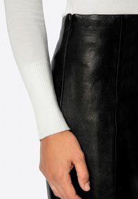 Gonna in pelle nera dalla texture liscia, con cerniera laterale e silhouette aderente. Polsino di maglione bianco a coste parzialmente visibile.