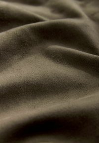 Olive rohelise kangaga, pehme ja sileda tekstuuriga, mis kuvab peeneid voltide ja lainete mustreid, rõhutades selle paindlikkust ja kergust.