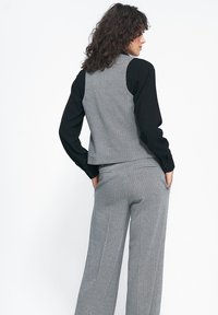 Szary kamizelka w wzór hounds-tooth zestawiona z czarną bluzką z długim rękawem i dopasowanymi spodniami. Tkanina wygląda na gładką z klasycznym, dopasowanym krojem.