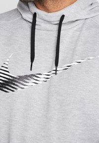 Sweat à capuche gris avec un logo Nike en forme de virgule à rayures noires et blanches et des cordons noirs visibles sur la partie supérieure de la poitrine et du cou.