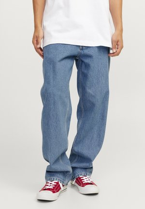 Jeans de denim azul claro con un corte relajado, costuras prominentes y un diseño de pierna recta, combinados con zapatillas rojas y blancas.