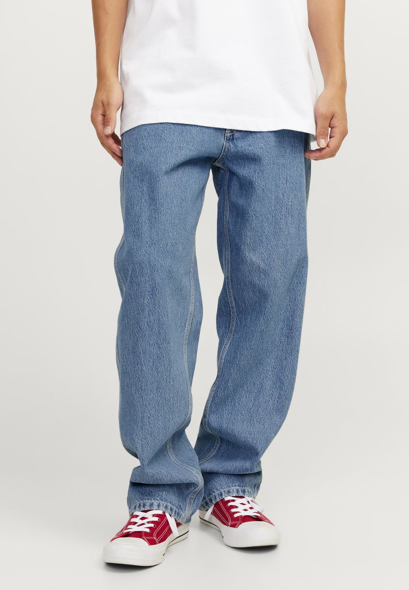 Jeans de denim azul claro con un corte relajado, costuras prominentes y un diseño de pierna recta, combinados con zapatillas rojas y blancas.