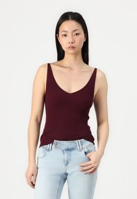 Top din bumbac burgund cu dungi, de tip tank, cu decolteu adânc în V și bretele late, asortat cu blugi de culoare albastru deschis, care au un buzunar frontal și accente metalice.