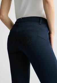 Vaqueros azul marino con una textura suave, que cuentan con un bolsillo trasero adornado con bordado de cuentas negras en un diseño en cursiva.