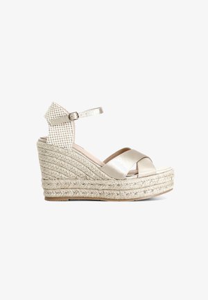 Sandalia de cuña beige con suela de yute trenzada, diseño de tiras cruzadas y correa en el tobillo tejida con cierre de hebilla. Acabado suave y brillante.