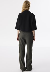 Czarna skórzana kurtka z krótkimi rękawami, zestawiona z oliwkowymi spodniami cargo z bocznymi kieszeniami i prostym krojem nogawek.