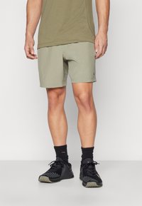 Khaki athletic shorts with a smooth texture, featuring a small black logo. Paired with black sneakers and crew socks.