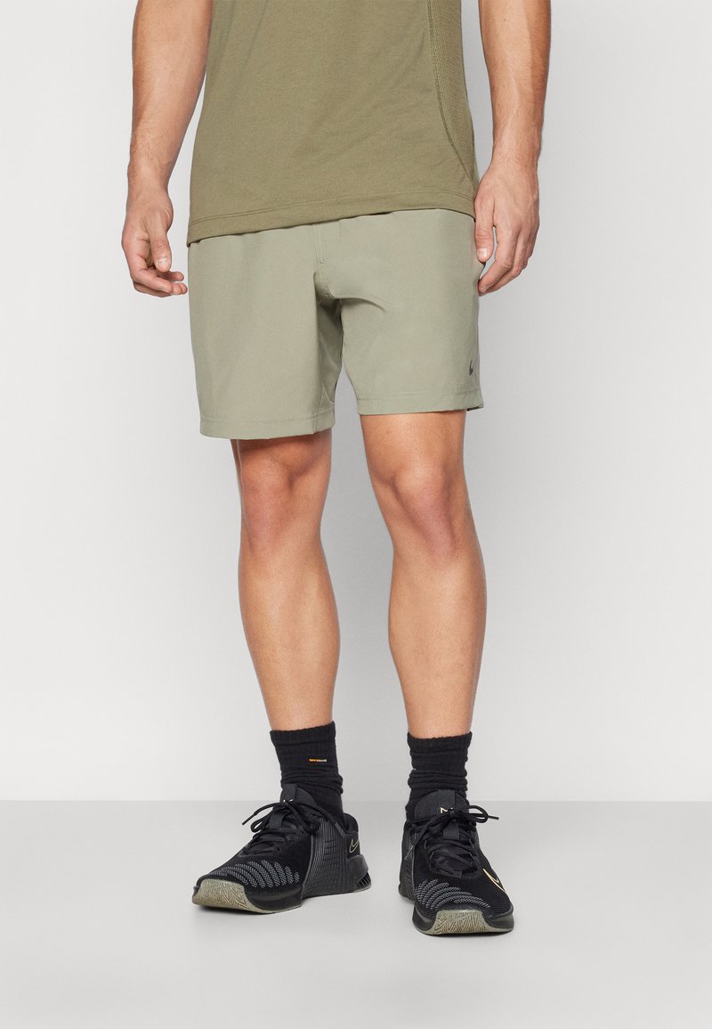 Khaki athletic shorts with a smooth texture, featuring a small black logo. Paired with black sneakers and crew socks.