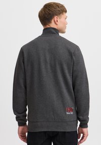 Hall triiksärk kõrge kraega, soonikkoes mansettide ja äärega. Alumise parema serva lähedal on punase tikitud logotekst. Sile tekstuur.