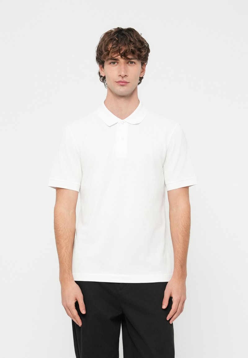 Λευκό πόλο πουκάμισο με κλασικό γιακά, κοντά μανίκια και διακριτικό λογότυπο στο στήθος. Κατασκευασμένο από μαλακό βαμβακερό ύφασμα.