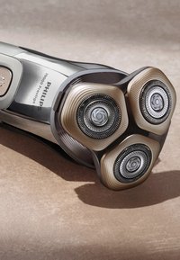 Philips elektrisch scheerapparaat met drie ronde gouden en zilveren koppen, ribbelstructuur op de randen en een metallic afwerking op het lichaam.