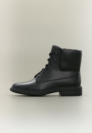 Bottine en cuir noir avec laçage à l'avant, col rembourré et petit talon empilé sur fond neutre.