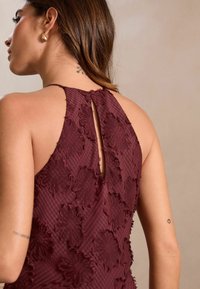 Maroon klänning med broderad blommönster, nyckelhål bakstängning och vertikalt randigt mönster. Slät yta med subtil lyster.