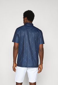 Polo shirt marine à motif losange texturé et accents clairs, avec un col et des manches courtes, associé à un short blanc.