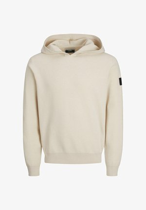 Beżowa bluza z kapturem o gładkiej fakturze, z prążkowanymi mankietami i dołem oraz małą czarną naszywką z logo na lewym rękawie.