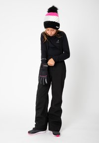 Pantalons de ski noirs, haut à manches longues et gants noirs avec des accents roses. Bonnet en tricot noir, blanc et rose avec un pompon dessus.