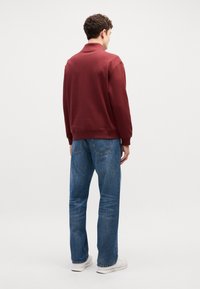 Μαρόν φούτερ με ριμπ λαιμό, συνδυασμένο με ανοιχτό μπλε τζην παντελόνι. Λευκά sneakers ολοκληρώνουν την εμφάνιση. Πίσω όψη.