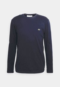 Navy long-sleeve t-shirt made of cotton with a crew neckline, features a small green embroidered logo on the chest. Smooth texture.