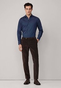 Navyblauw geruit overhemd met knopen en lange mouwen, gecombineerd met donkerbruine corduroy broek en donkere leren schoenen.