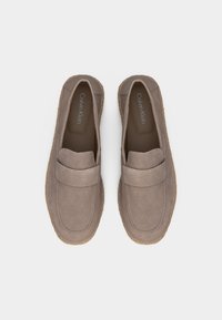 Ζευγάρι loafers από σουέντ σε ταουπέ χρώμα, χωρίς κορδόνια, με ραμμένες σόλες και το λογότυπο Calvin Klein στο εσωτερικό, εμφανιζόμενα από πάνω σε λευκό φόντο.
