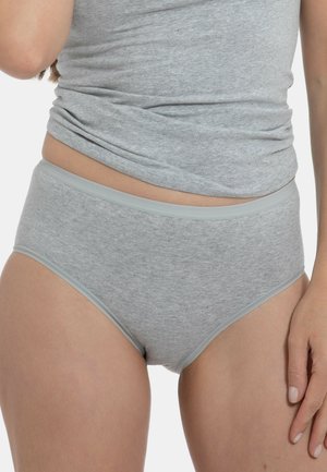 Frau trägt hellgraue Baumwoll-Slips mit hohem Bund und ein passendes eng anliegendes Tanktop, steht mit einer Hand entspannt an ihrer Seite.