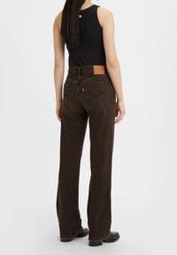 Pantalones vaqueros de pierna ancha marrones, hechos de denim, con un parche de marca de cuero en la parte trasera, detalles de bolsillo cosidos y un corte relajado.