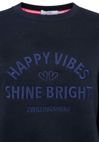 Navyblaues Sweatshirt mit geripptem Kragen und gesticktem Text "HAPPY VIBES SHINE BRIGHT" in dunklerem Blau, umrahmt von zwei Herzformen.