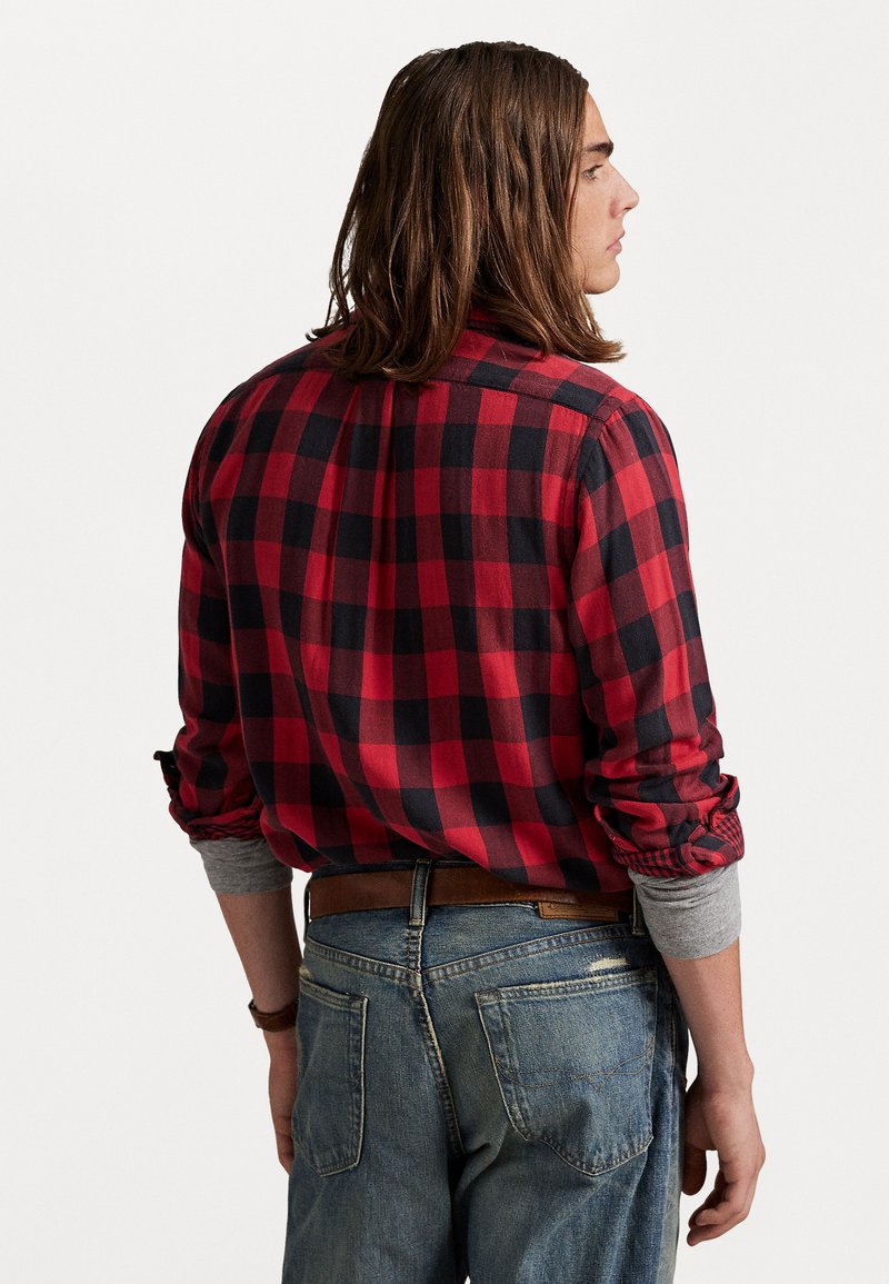 Rød og sort ternet flannel skjorte med lange ærmer og opfoldede manchetter, parret med udvaskede blå jeans og et brunt læderbælte.