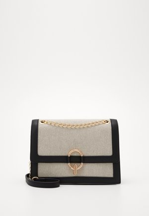 Rechteckige beige Stoffhandtasche mit schwarzen Lederkanten, goldenem Kettendetail oben und einem goldenen runden Verschluss vorne.