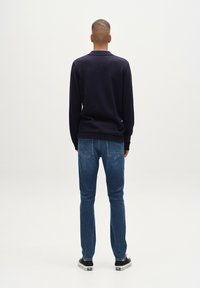 Mornarsko pleteno pulover s ovratnikom, v kombinaciji z svetlo modrimi kavbojkami in črnimi čevlji. Gladka tekstura, prilegajoč dizajn in čiste linije.