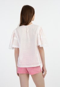 Blusa bianca con maniche corte a volant, con motivo a pois rosa e arancio e bordatura in pizzo, abbinata a pantaloni corti in denim rosa.